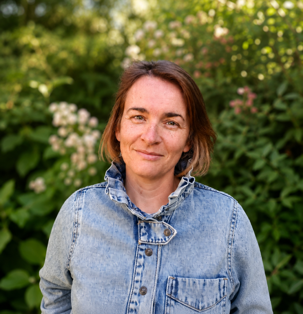 Céline en veste en jean, souriante, devant une haie fleurie